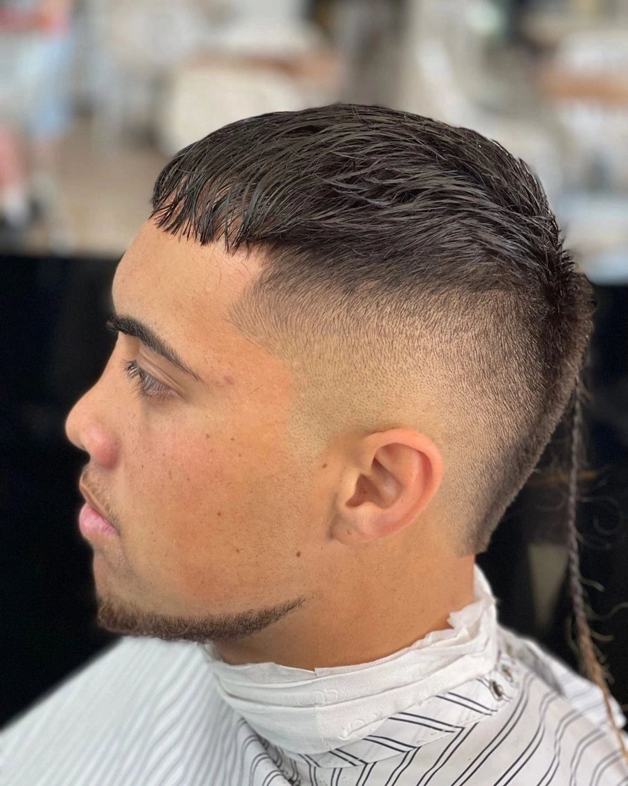 Side profile of a young man with a textured fringe, a skin fade and a sharp beard line.