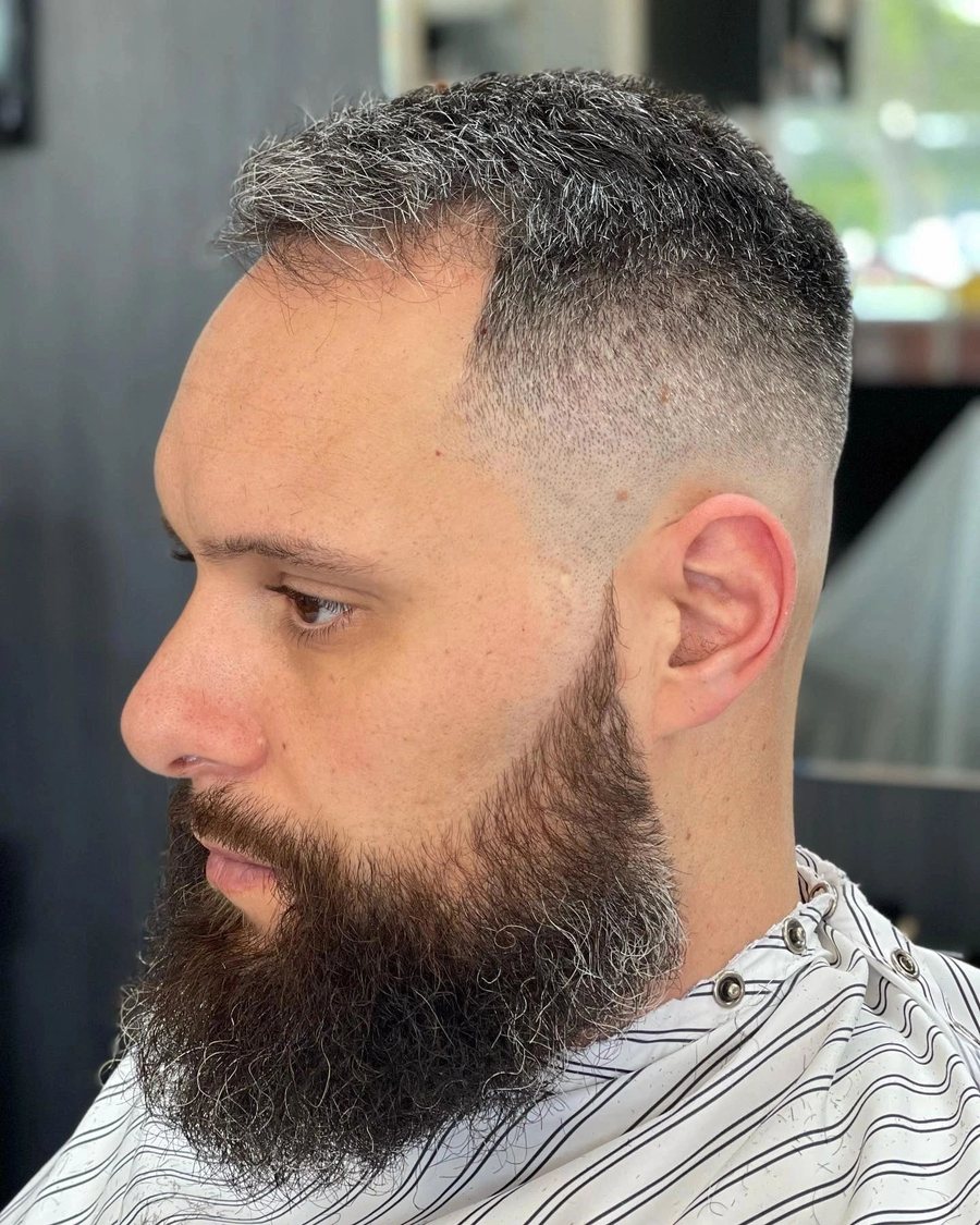 Side profile of a man with a full beard blended into a high skin fade.