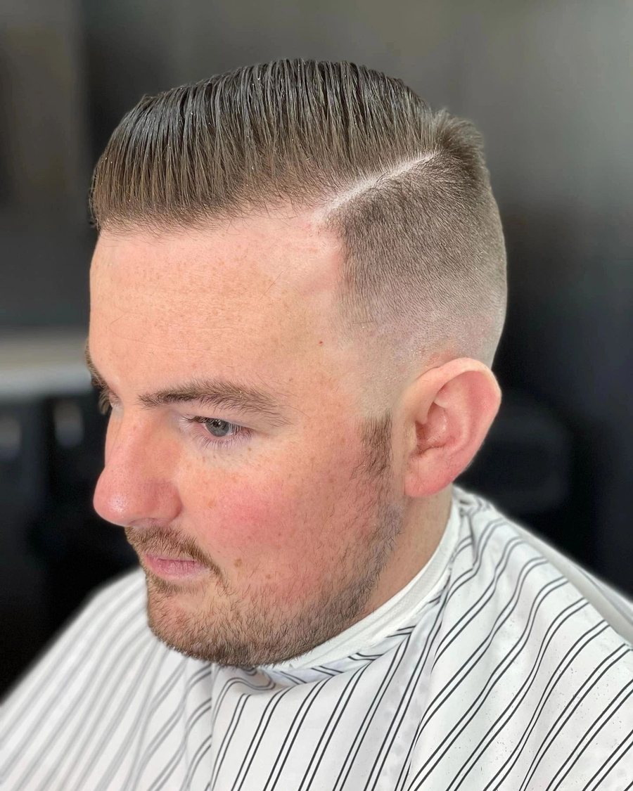 Side profile of a man with a hard part, a side-swept top and a skin fade.