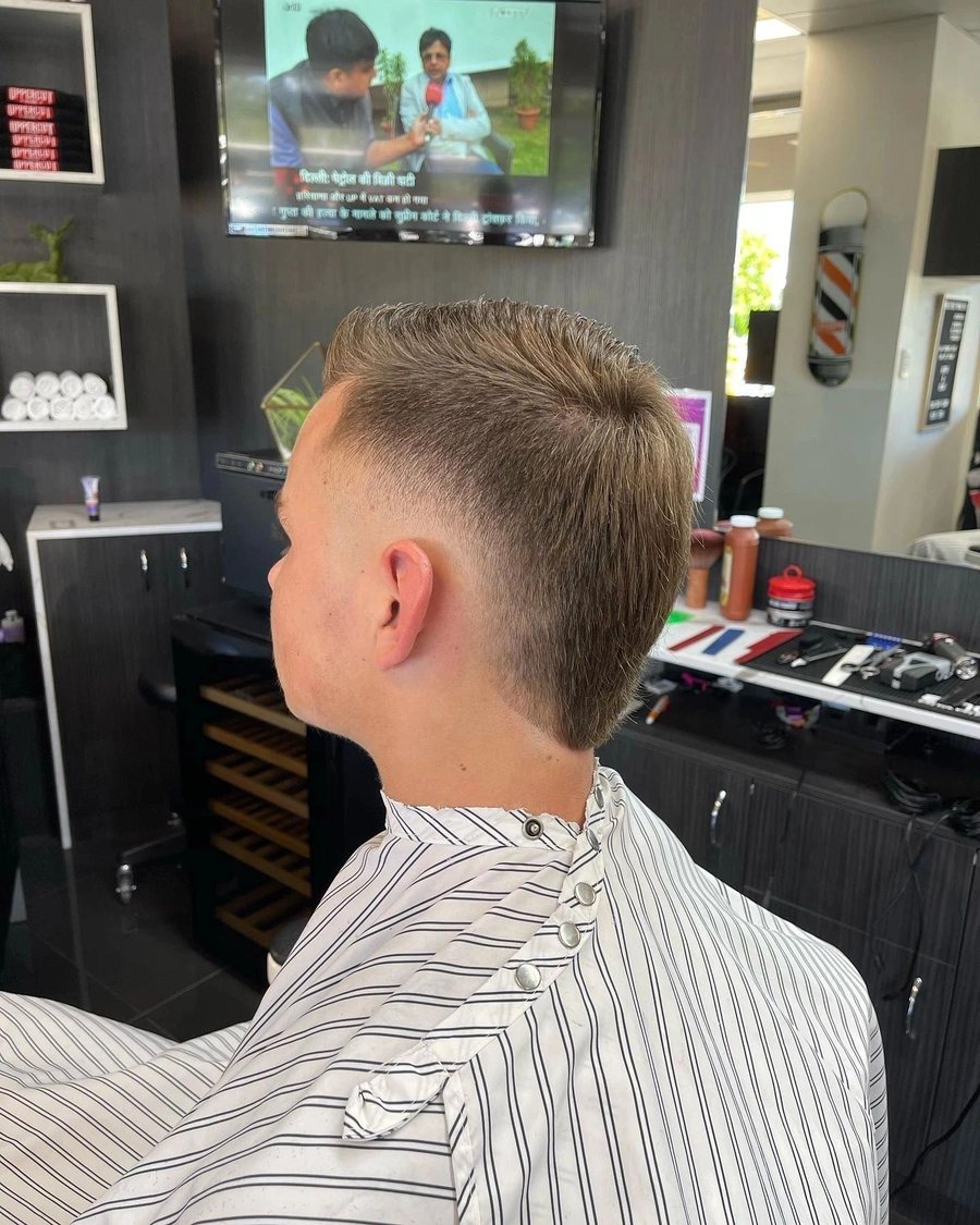 Back view of a taper fade, with the barber pole and product shelves behind.