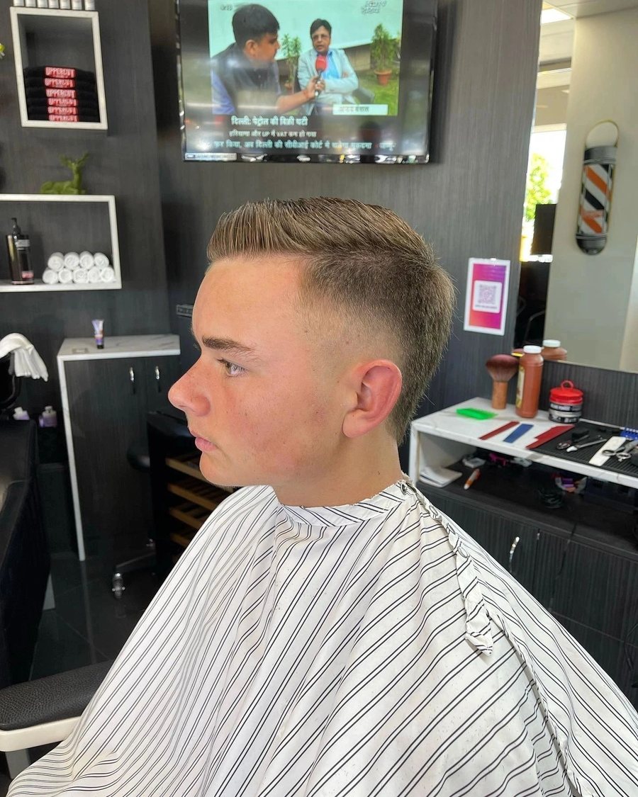 Young man in the chair with a fresh taper fade, the shop floor behind him.