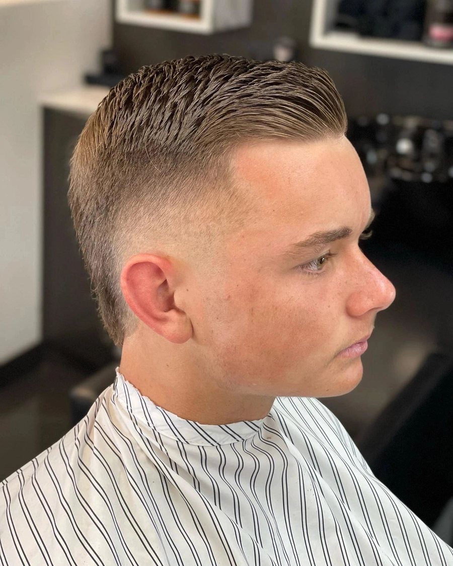 Side profile of a young man with a textured crop combed forward over a taper fade.